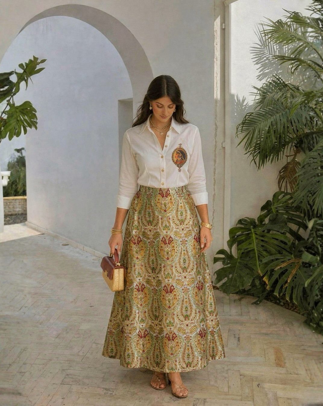 Woman wearing a white embroidered blouse and a long patterned gold and green skirt.