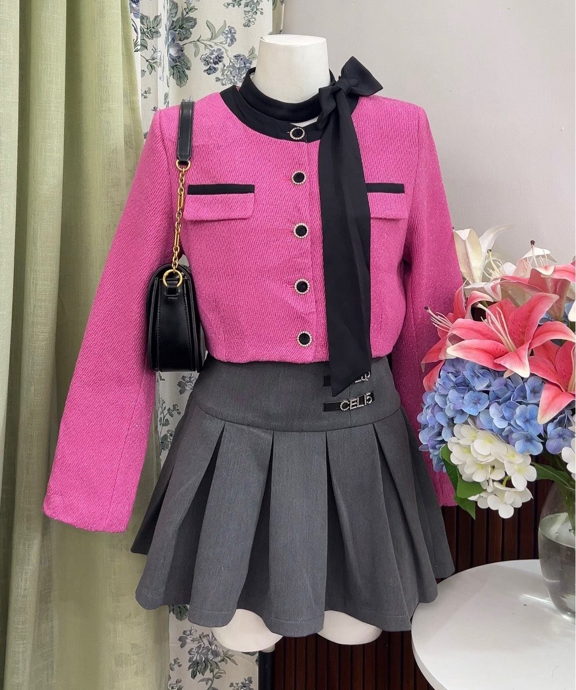 A pink textured jacket with black trim displayed on a mannequin with a grey pleated skirt.