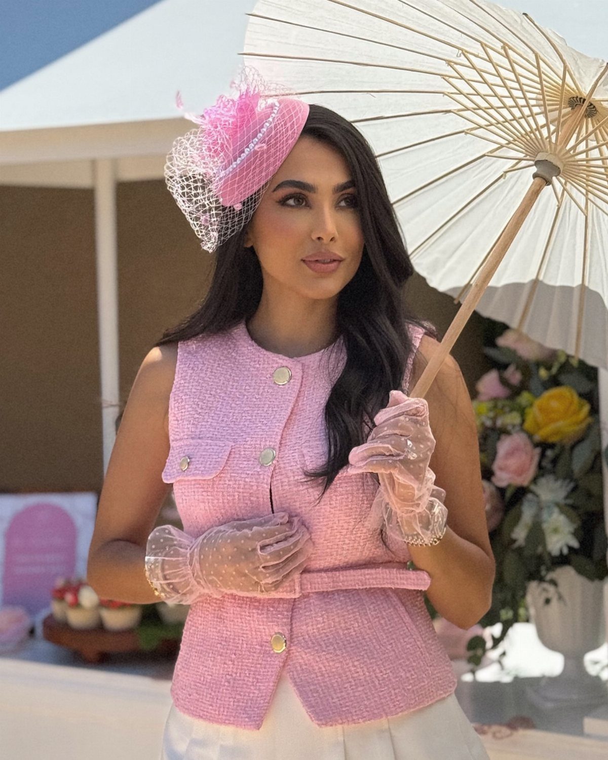 A woman wearing a pink tweed vest and a decorative pink and white fascinator hat.