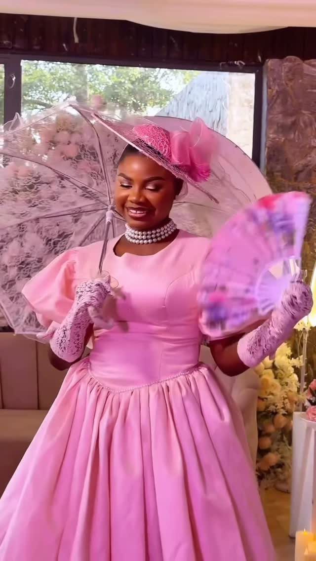 A woman in a pink satin gown holding a lace parasol and a pink fan.