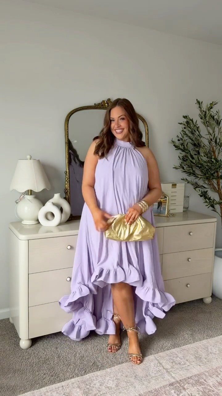 A smiling woman wearing a lavender high-low ruffled halter dress and gold clutch.