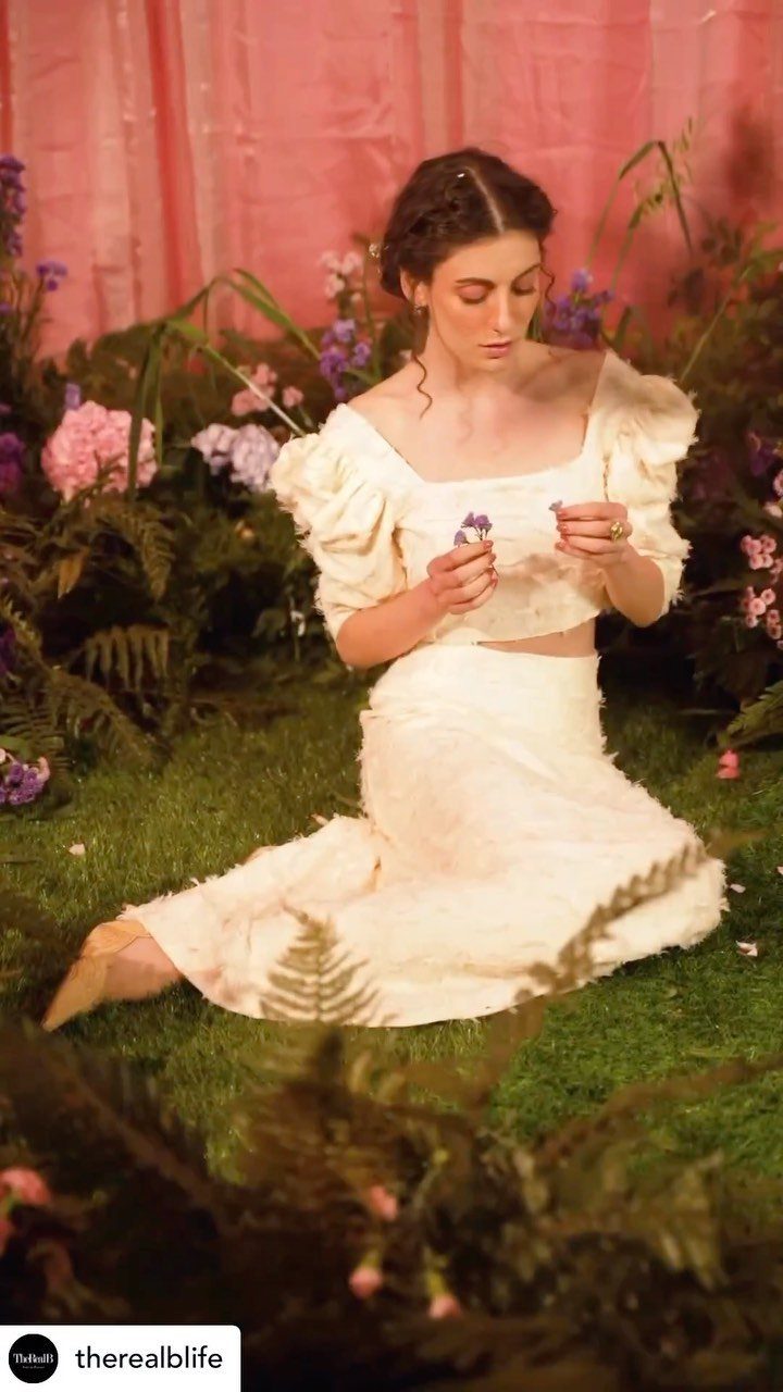 Woman in a cream puff-sleeved blouse and matching long skirt sitting in a garden.