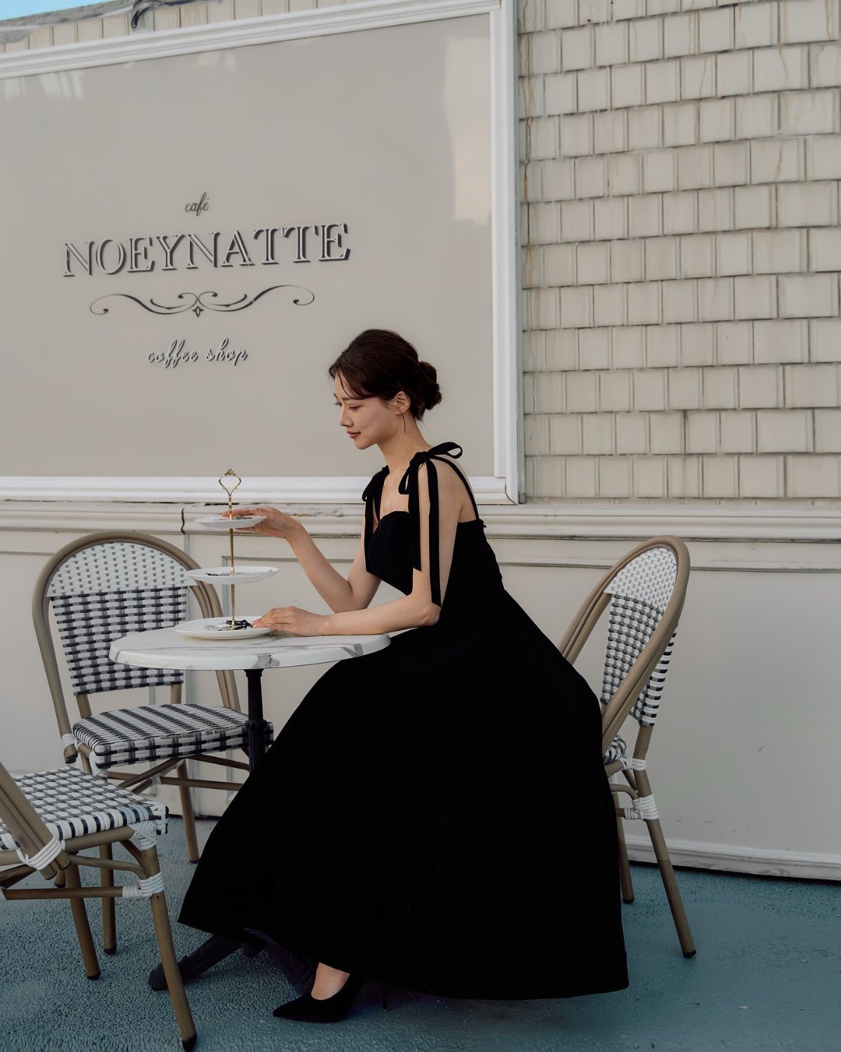 Woman in a black dress sitting at a cafe table with a tiered dessert stand.