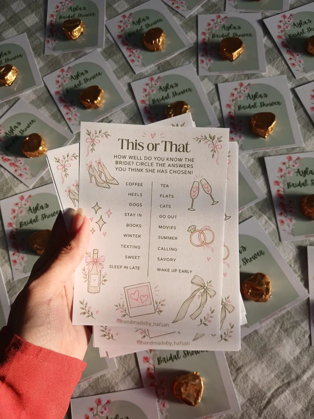 A hand holding a floral 'This or That' bridal shower game card over scattered party favors.