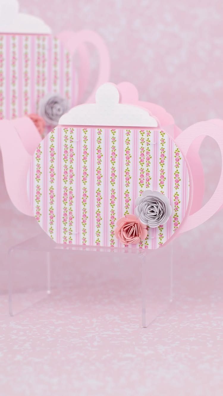 Pink striped teapot-shaped favor boxes decorated with small paper roses on a clear stand.