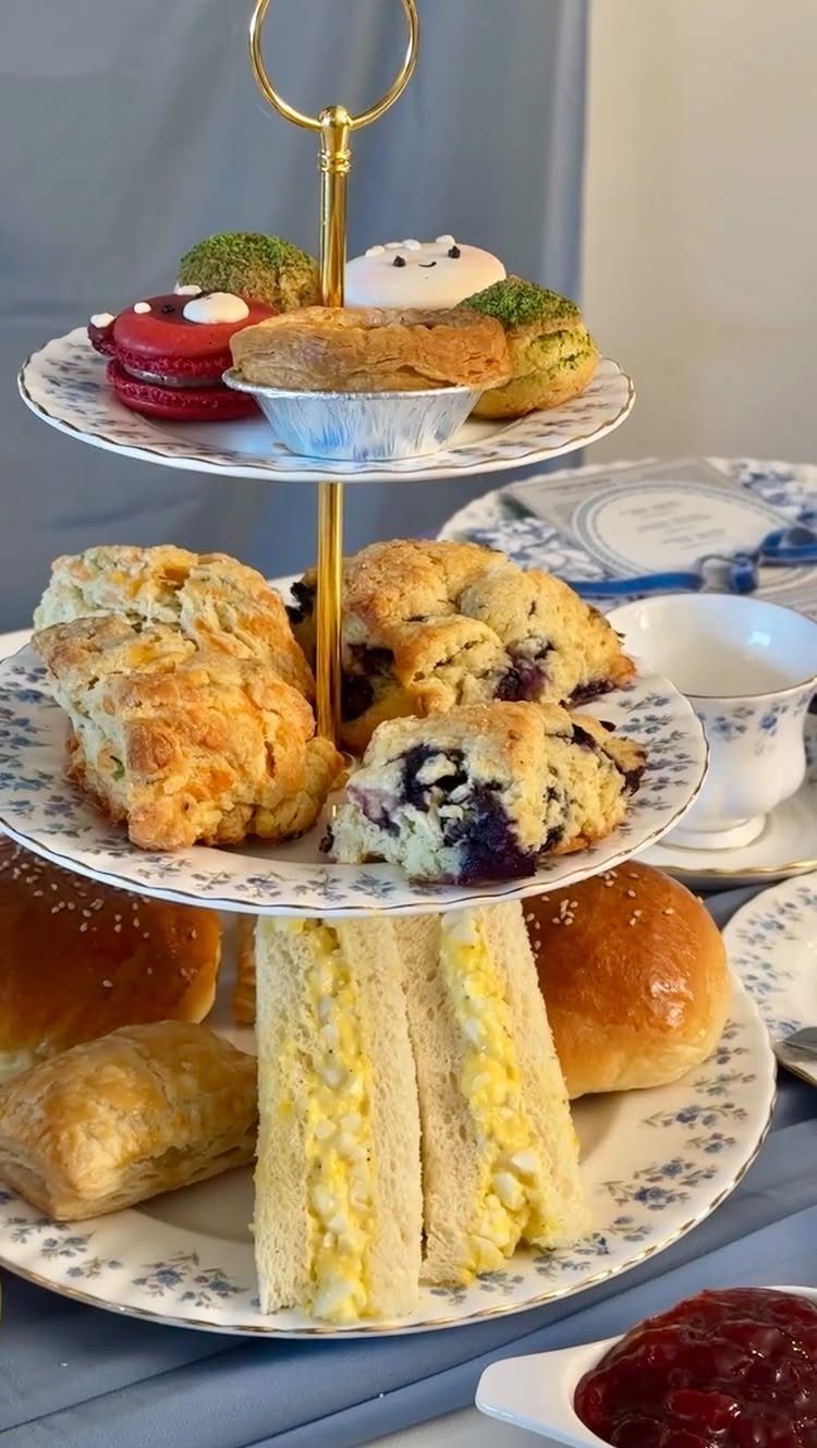 A three-tiered stand filled with macarons, blueberry scones, and egg salad sandwiches on floral plates.