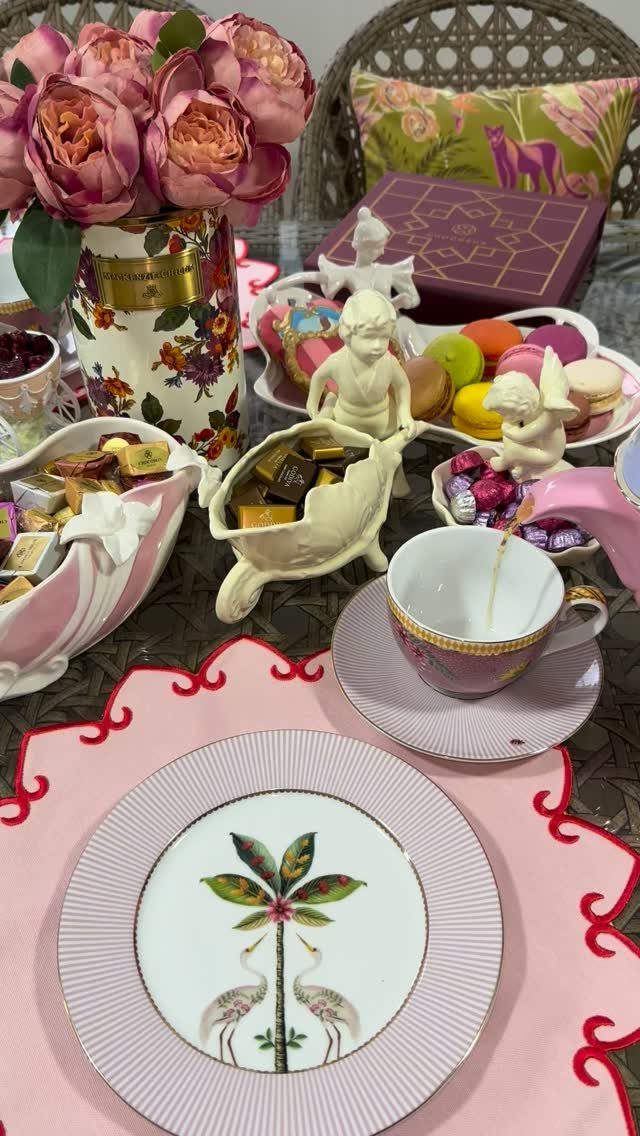 A decorated tea party table with pink roses, macarons, chocolates, and a crane motif plate.
