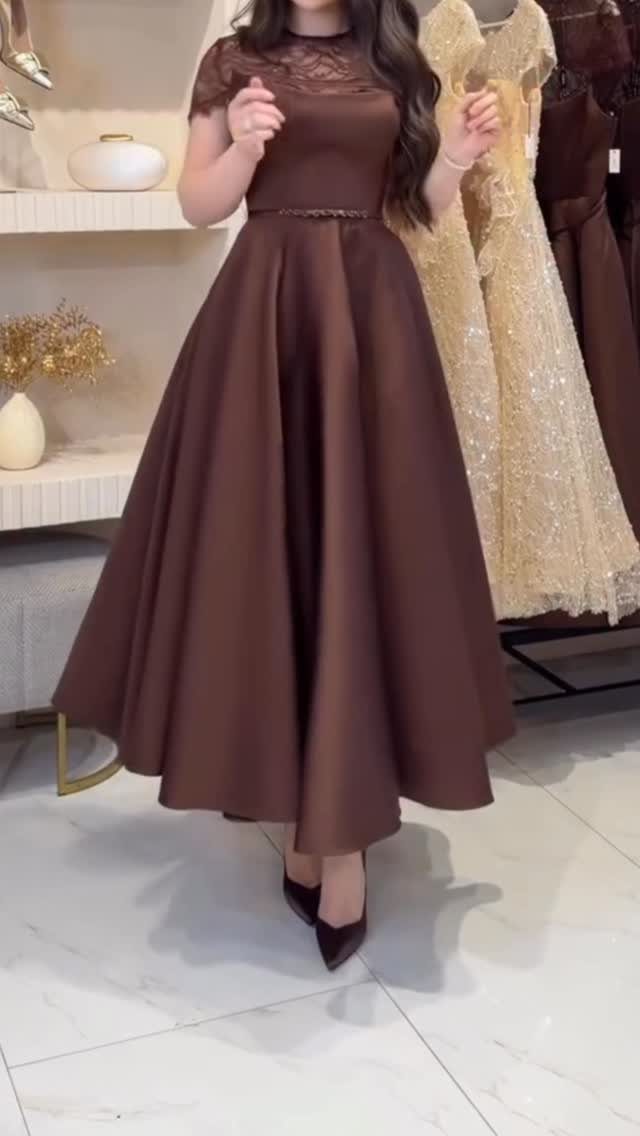 A woman posing in a brown satin midi dress with a lace bodice and full skirt.