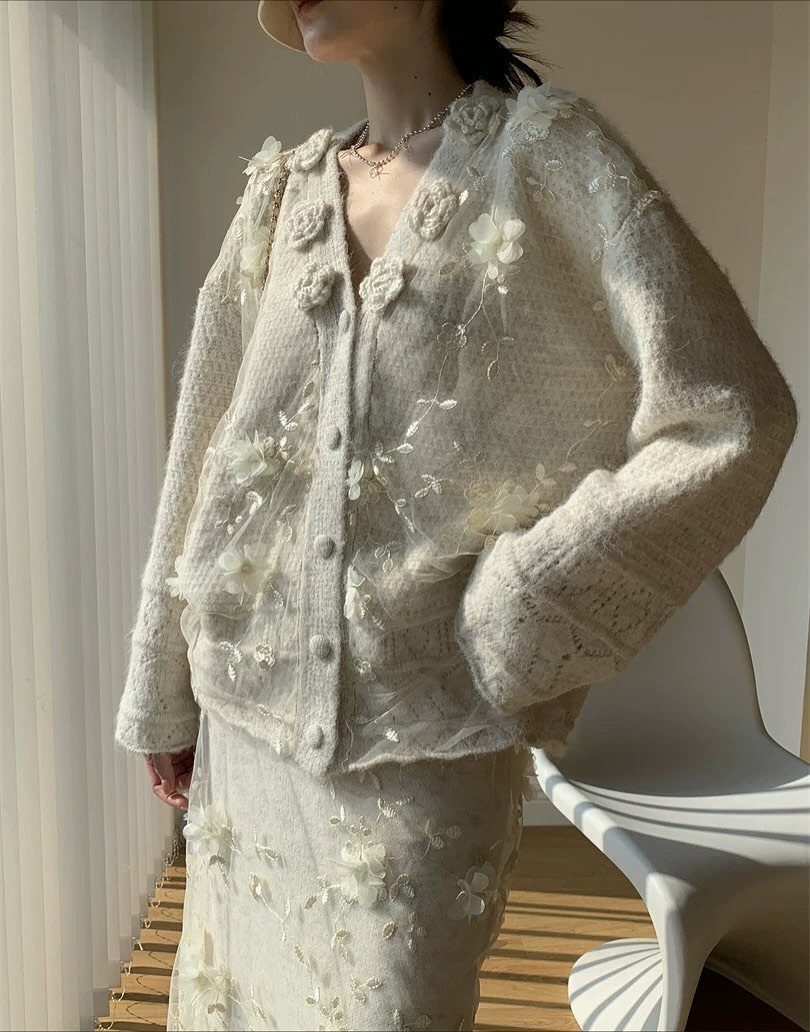 Person wearing a cream knit cardigan and skirt set with white floral embellishments.