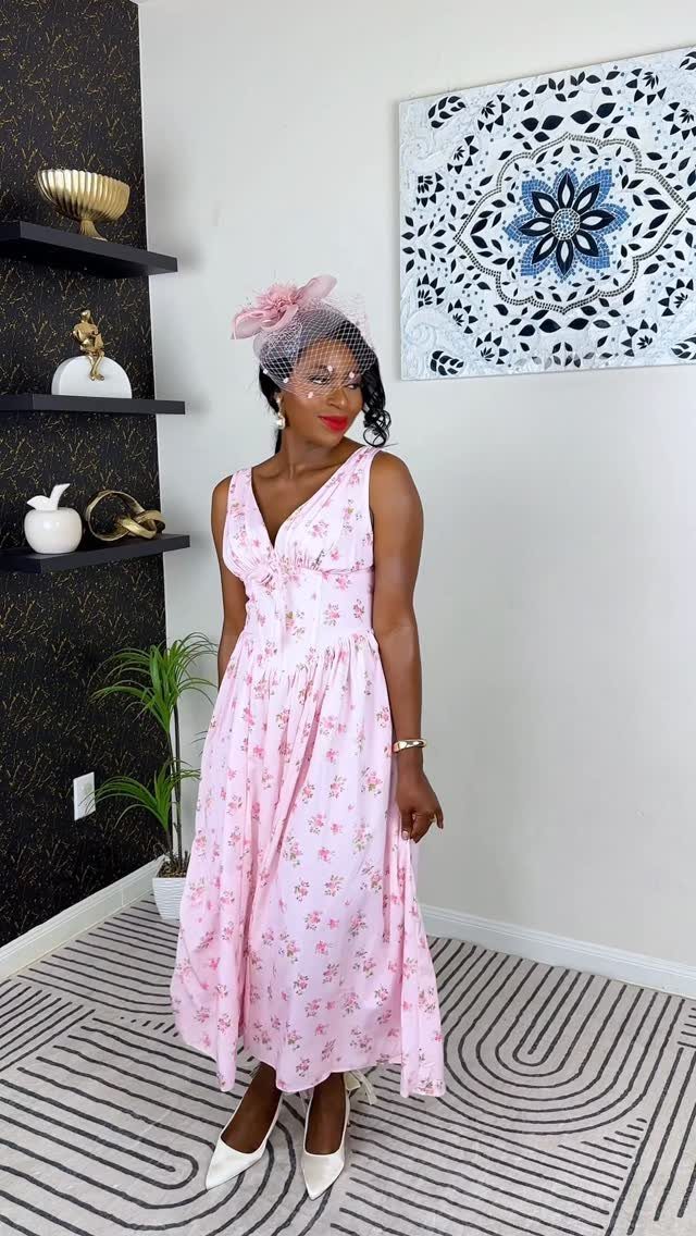 Woman in a pink floral midi dress and fascinator posing in a room.