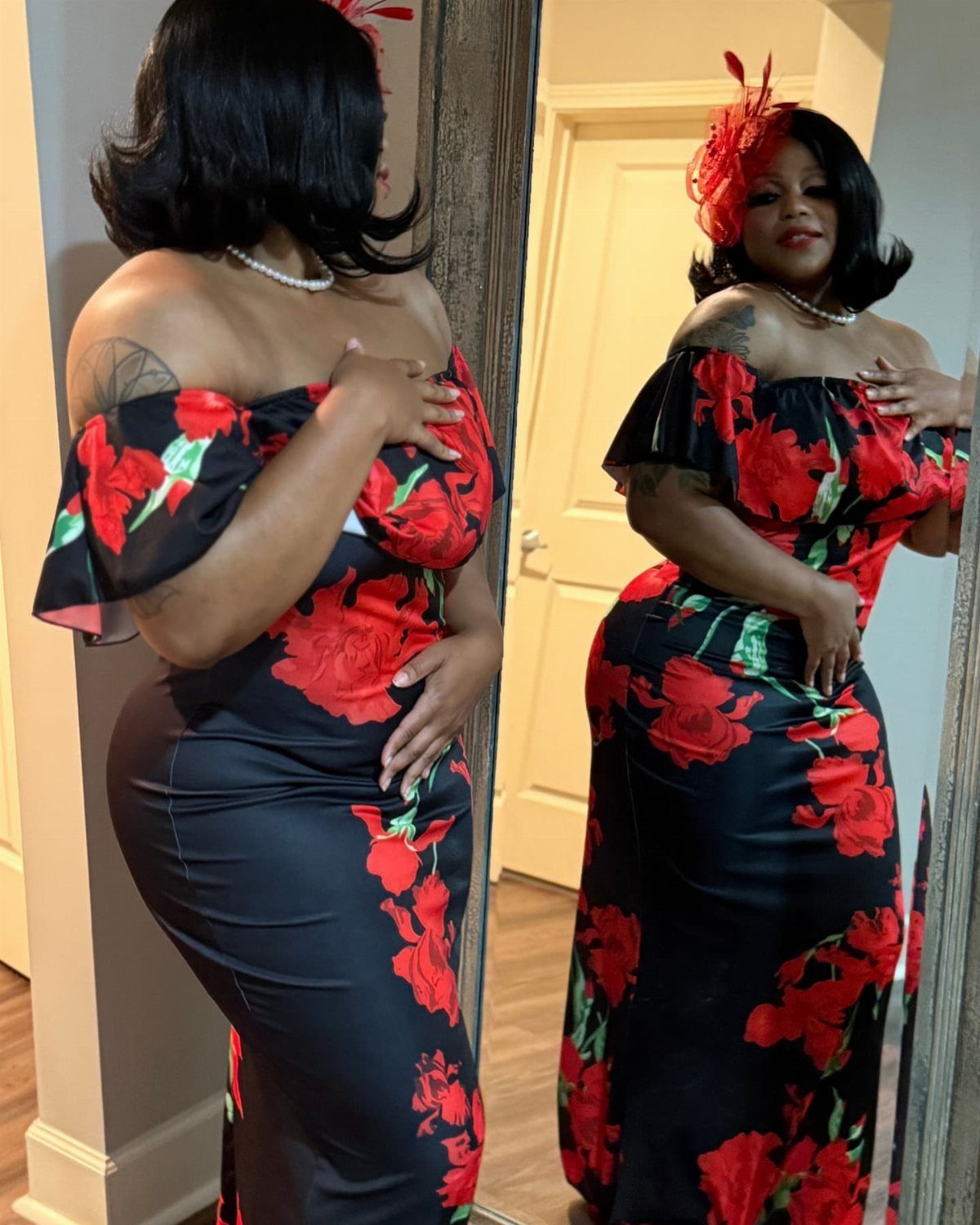 Woman in a black floral off-the-shoulder dress posing in front of a mirror.