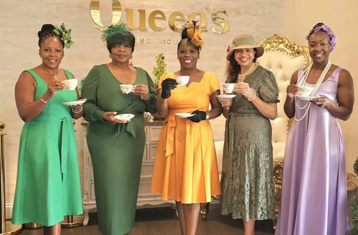 Five women in colorful dresses holding teacups and wearing elegant hats and jewelry.