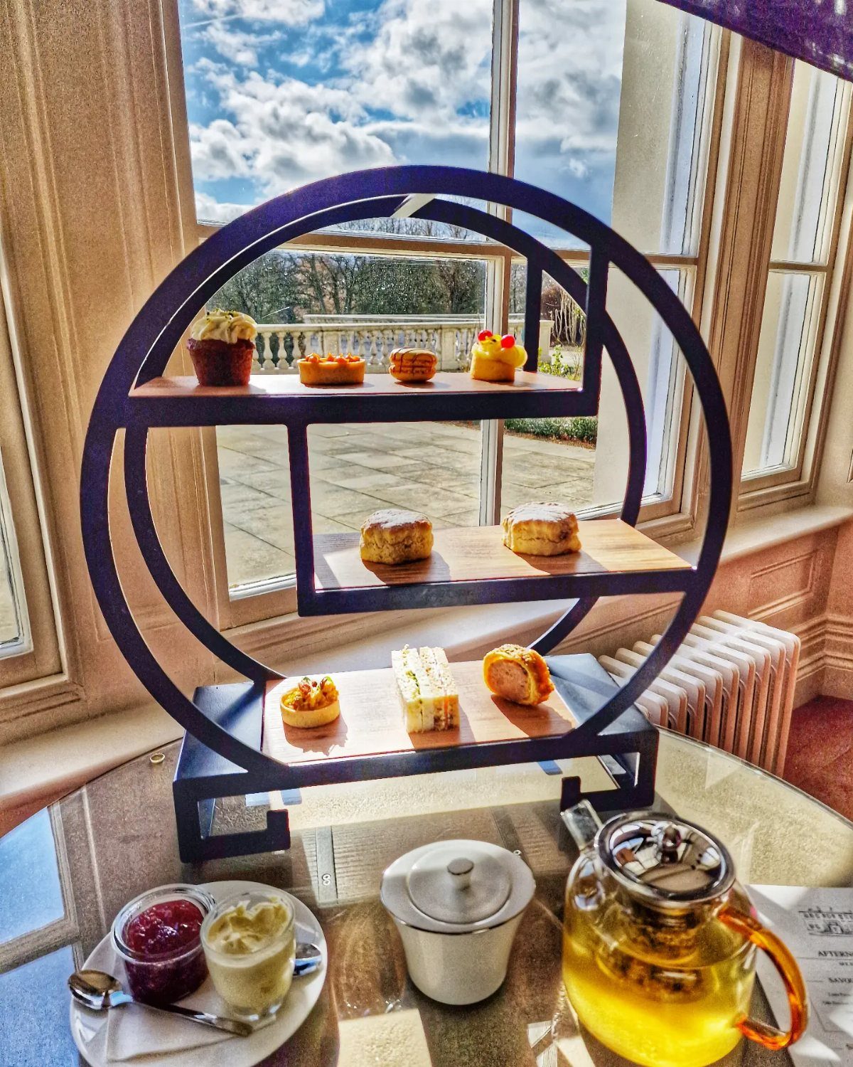 A tiered stand displaying pastries, scones, and sandwiches on a table near a window.