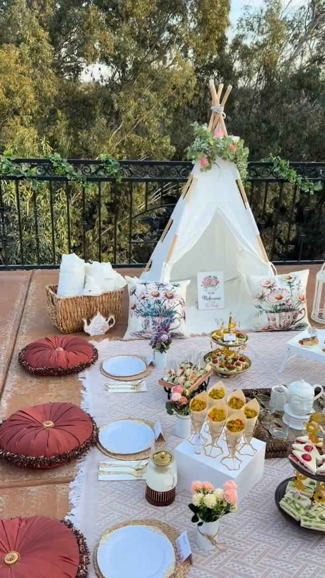 A white teepee and red velvet floor cushions arranged for an outdoor boho-style tea party.