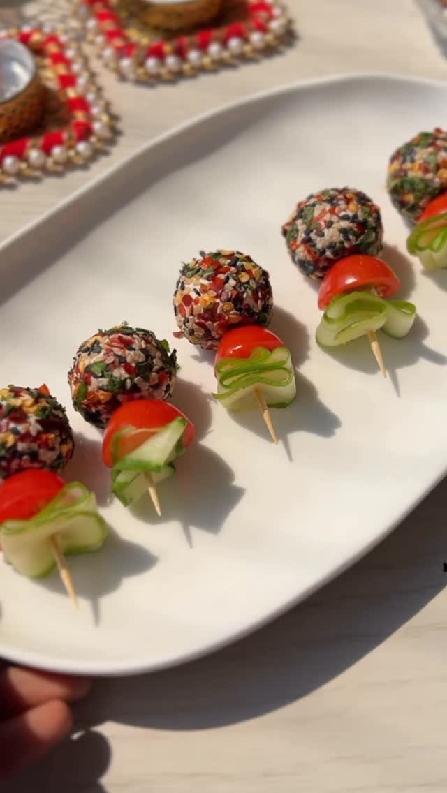 Savoury appetizers including herb-coated cheese balls and tomato cucumber bites on a white platter.