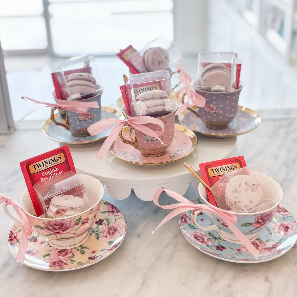 Teacups filled with macarons and tea packets, decorated with pink ribbons as party favors.