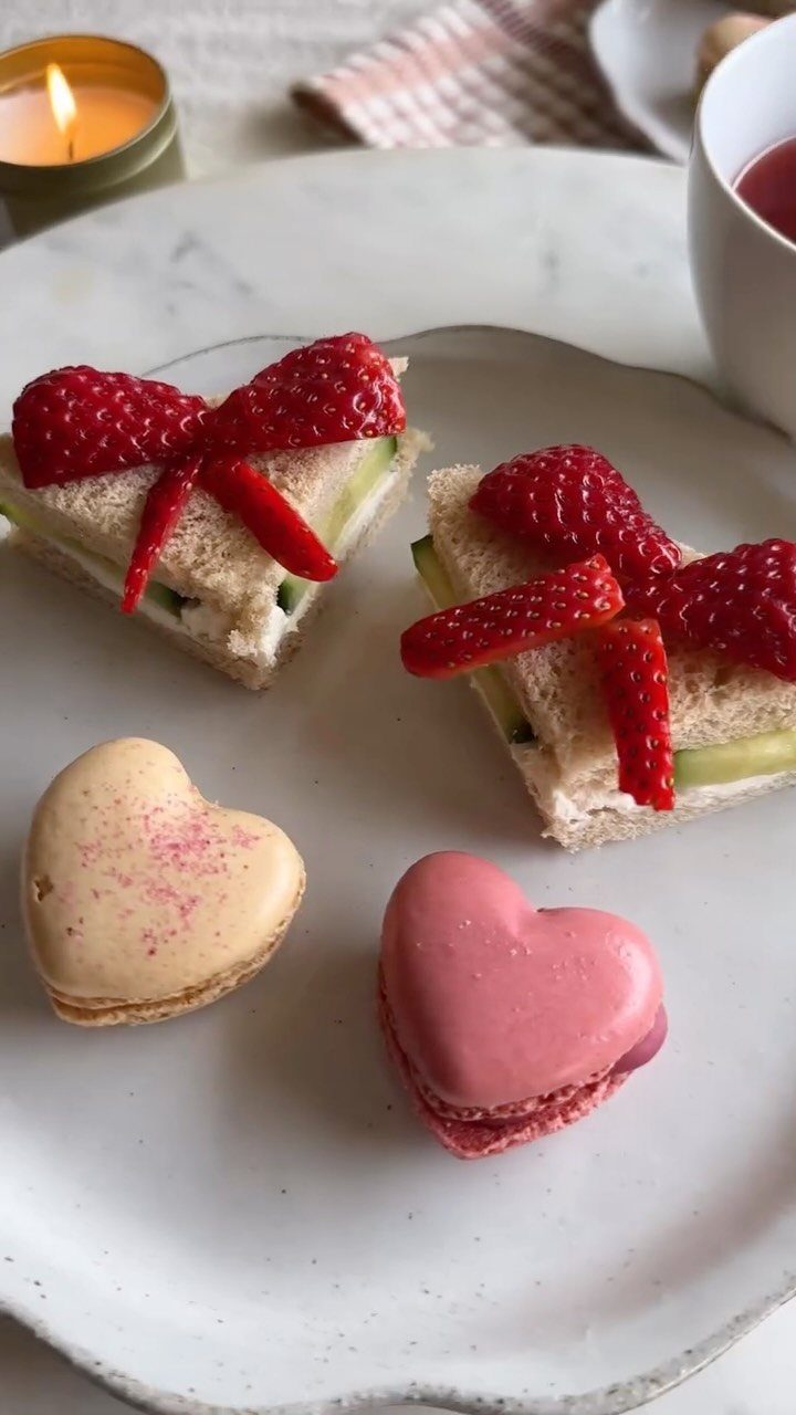 Heart-shaped strawberry sandwiches and macarons served on a white plate with a candle.