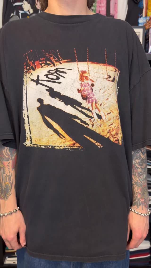 A person wearing a black Korn band graphic t-shirt with visible arm tattoos.