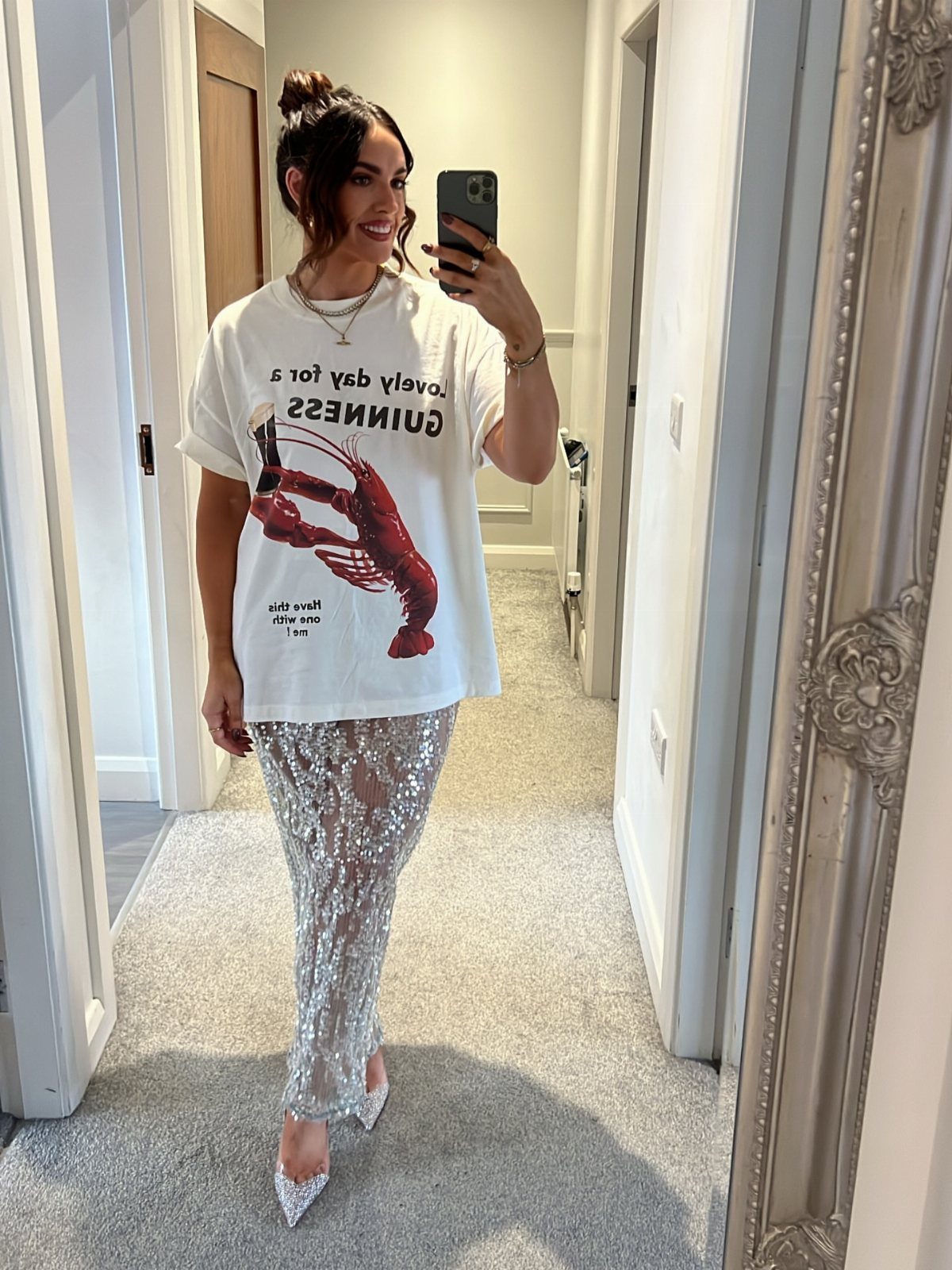 Woman in a white graphic t-shirt and silver sequined skirt posing for a mirror selfie.