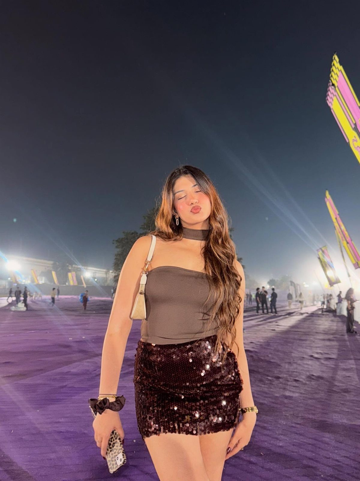 Woman in a brown strapless top and dark sequined miniskirt posing at night.