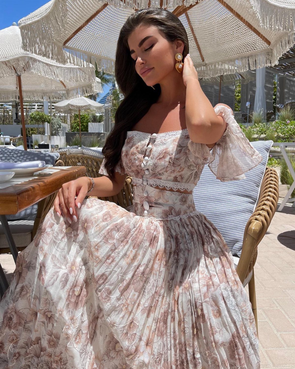 A woman wearing a floral two-piece outfit sitting at an outdoor cafe table.