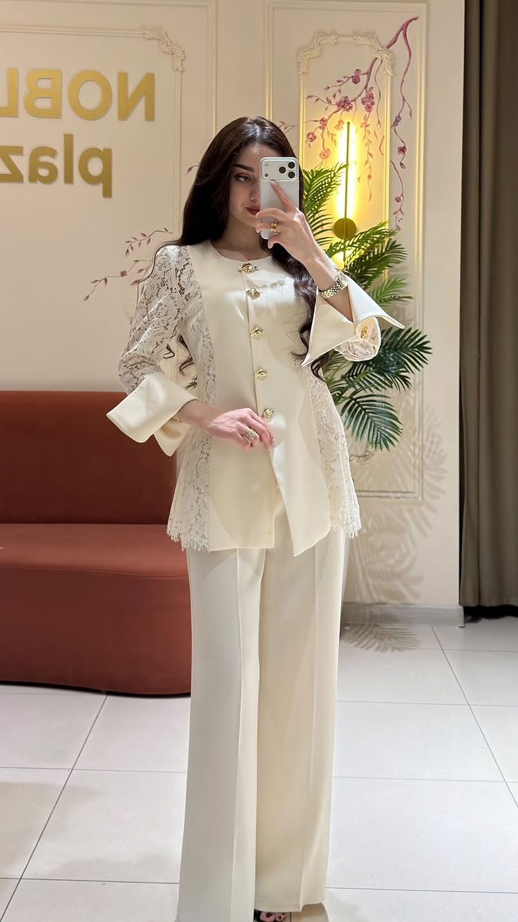 Woman in a cream lace two-piece outfit posing for a mirror selfie indoors.
