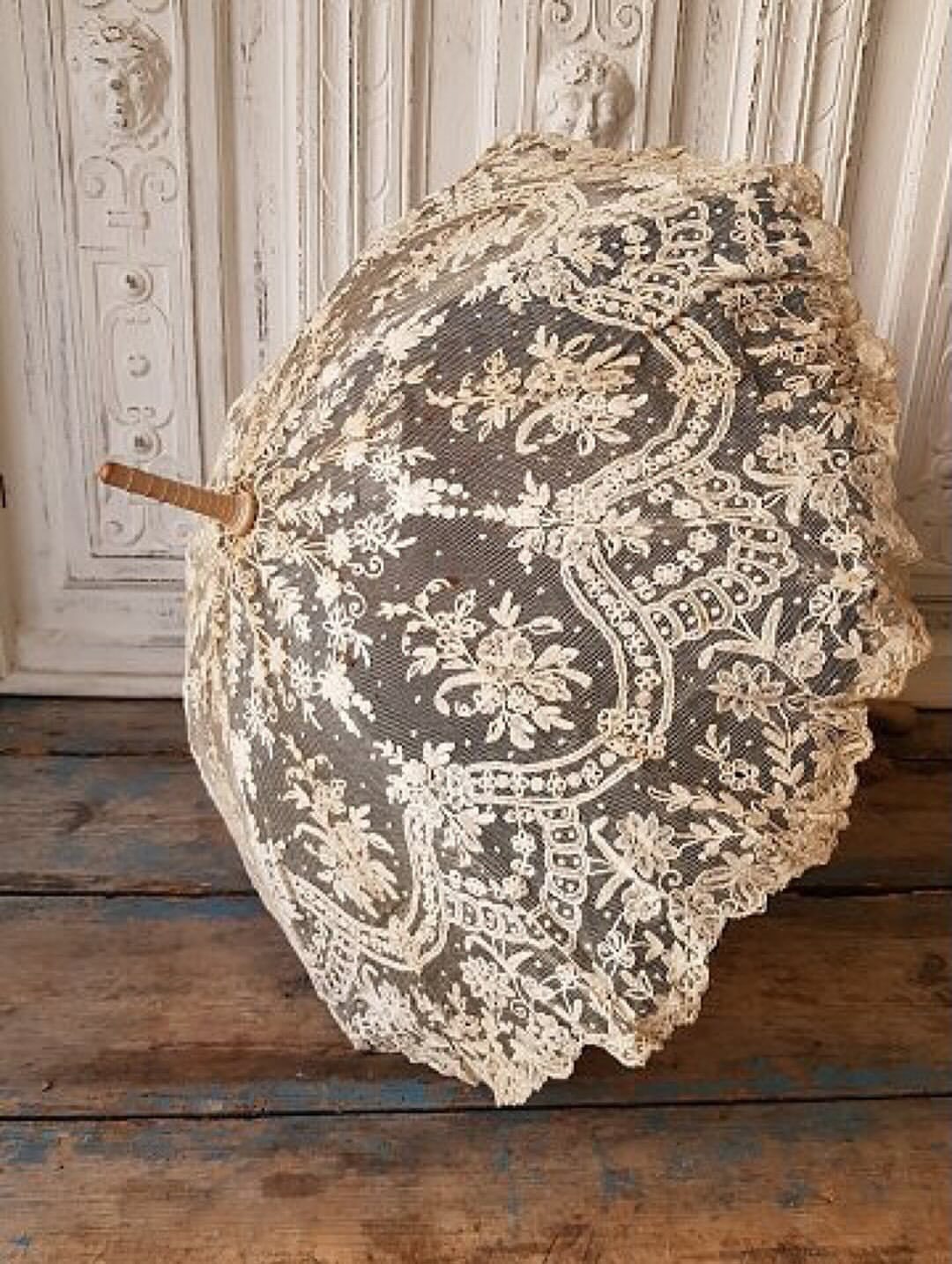 A vintage lace parasol with floral patterns resting on a rustic blue wooden floor.