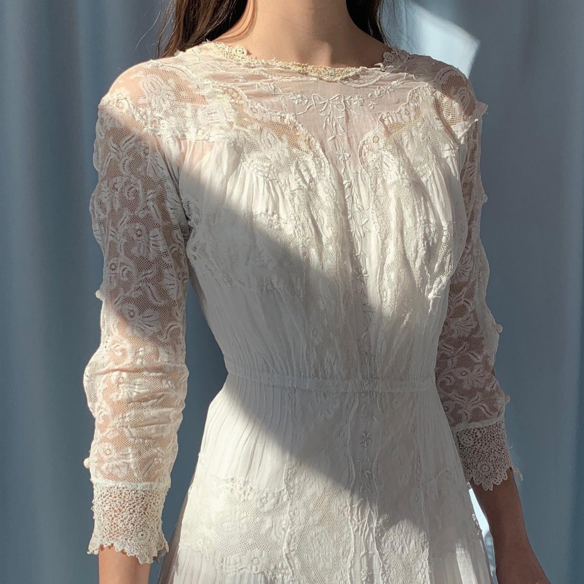 A person wearing an intricate white lace vintage-style dress with long sleeves.