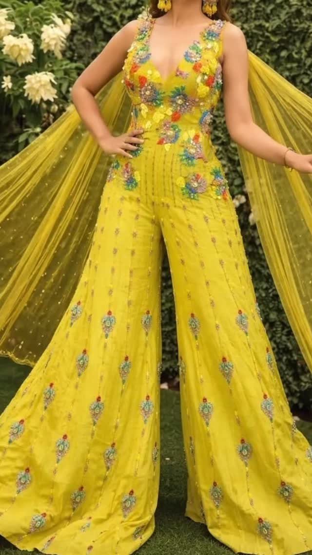 A person wearing a yellow floral embroidered jumpsuit with long sheer cape sleeves outdoors.