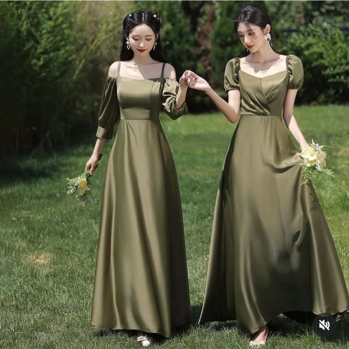 Two women in olive green satin dresses standing on a lush green lawn in a garden.