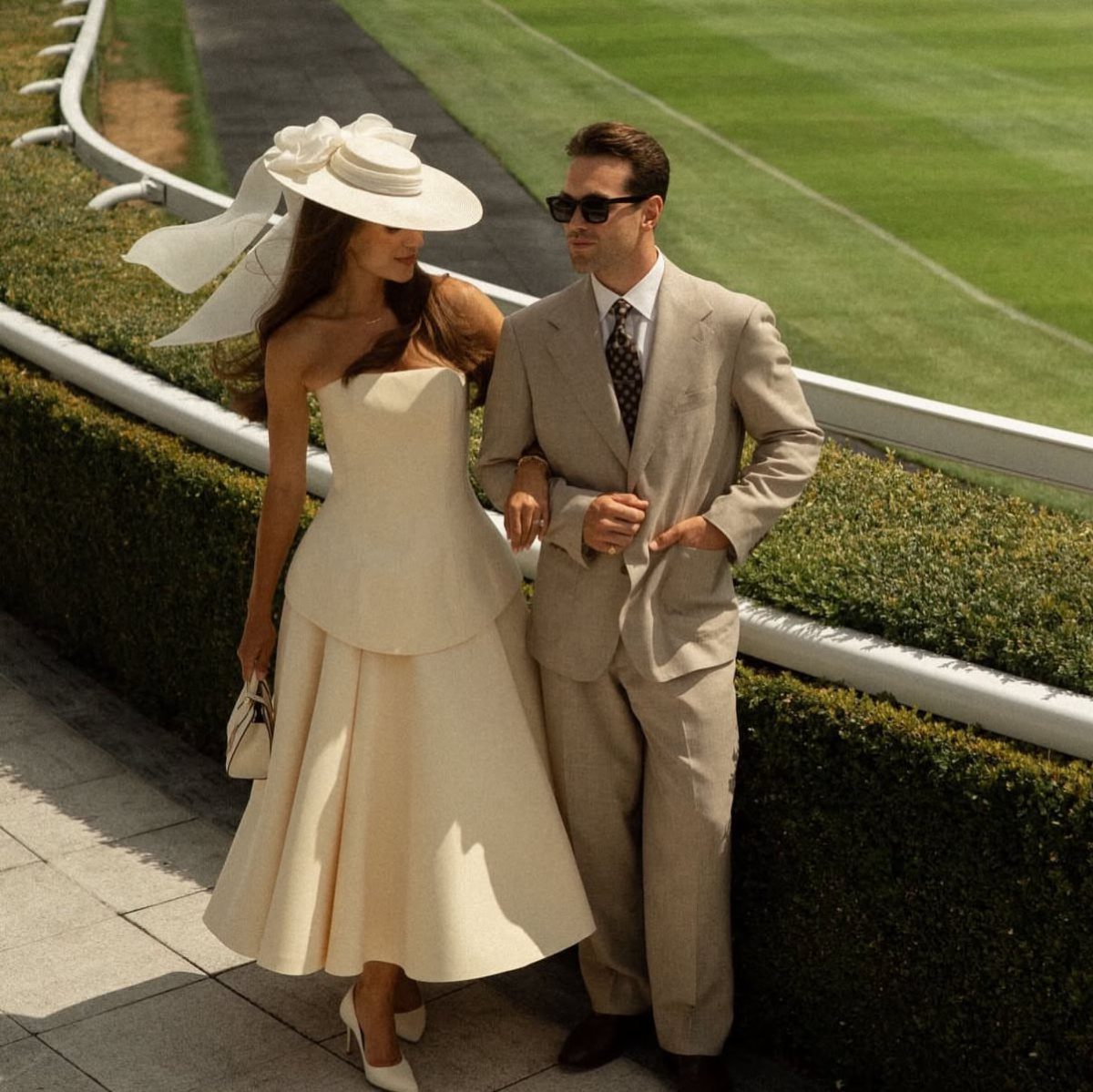 A woman wearing a cream dress and a large white wide-brimmed hat walking outdoors.