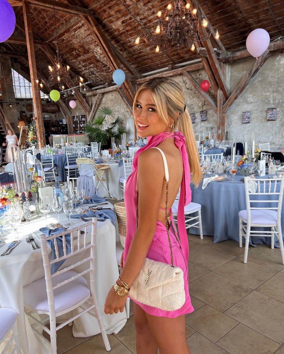 A smiling woman in a pink halter dress posing in a decorated rustic wedding venue.