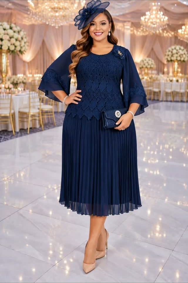 Woman in a navy blue lace and pleated midi dress posing in a ballroom.