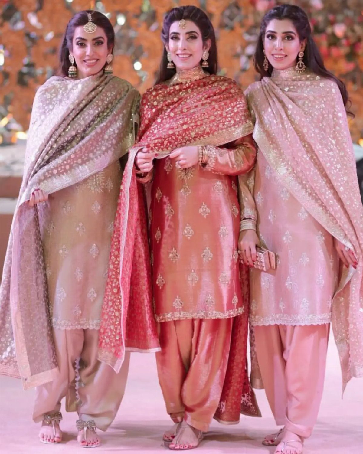 Three women posing in shimmering, embroidered traditional South Asian formal attire.
