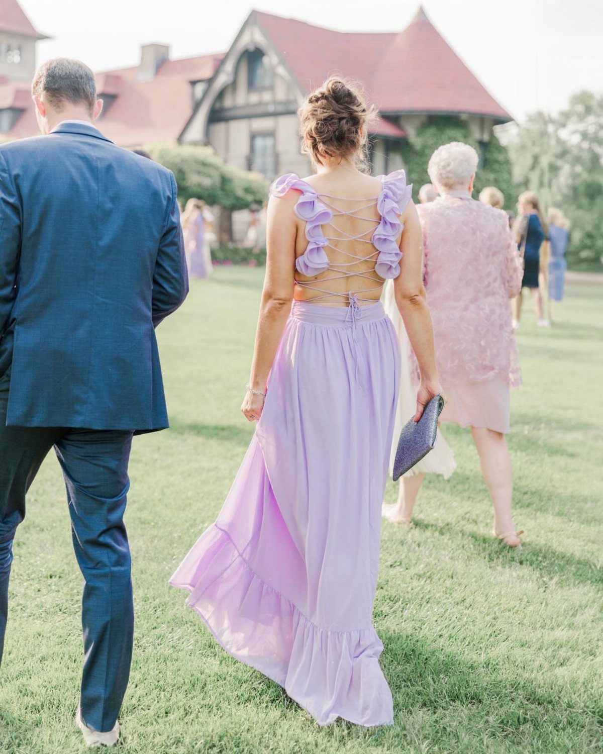 Woman in a long lavender ruffled dress walking across a green lawn at an outdoor event.
