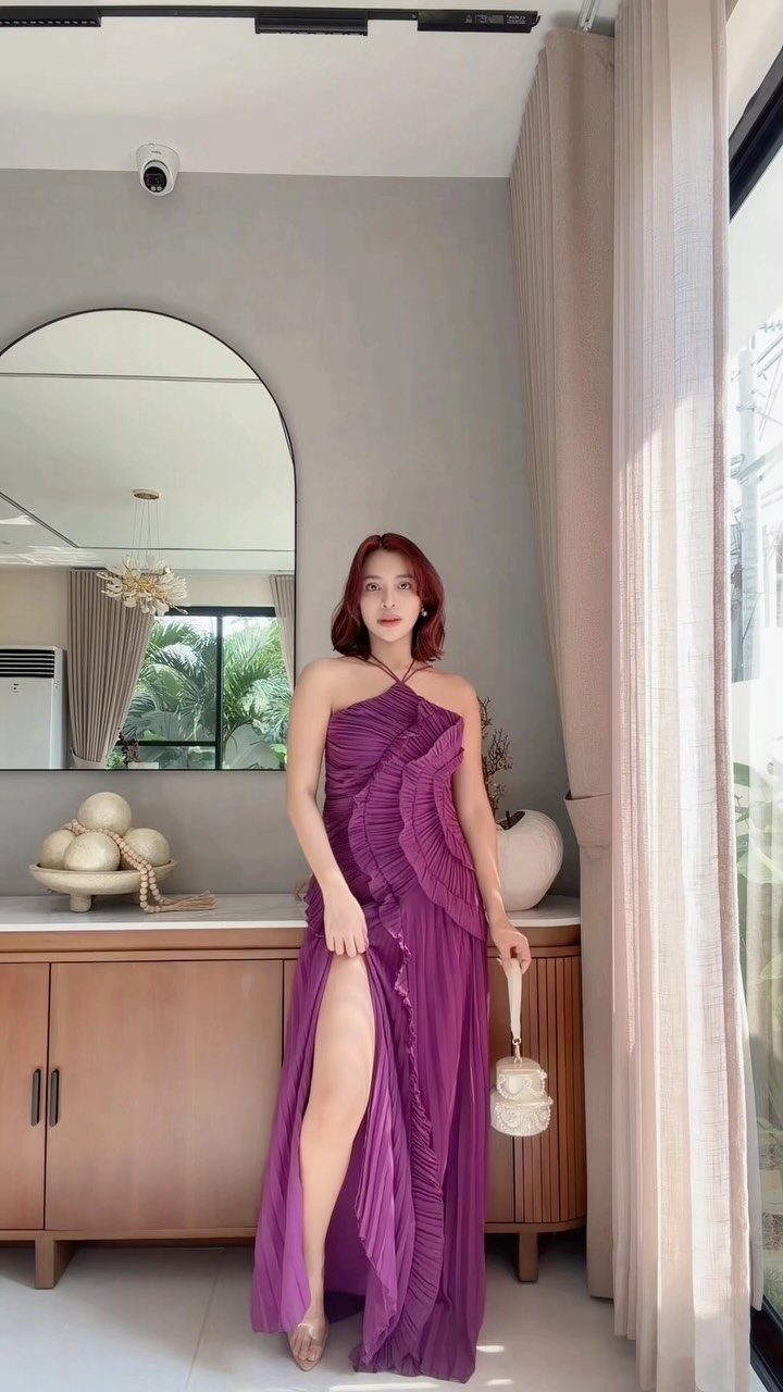 Woman in a long pleated purple halter dress posing in a bright room.