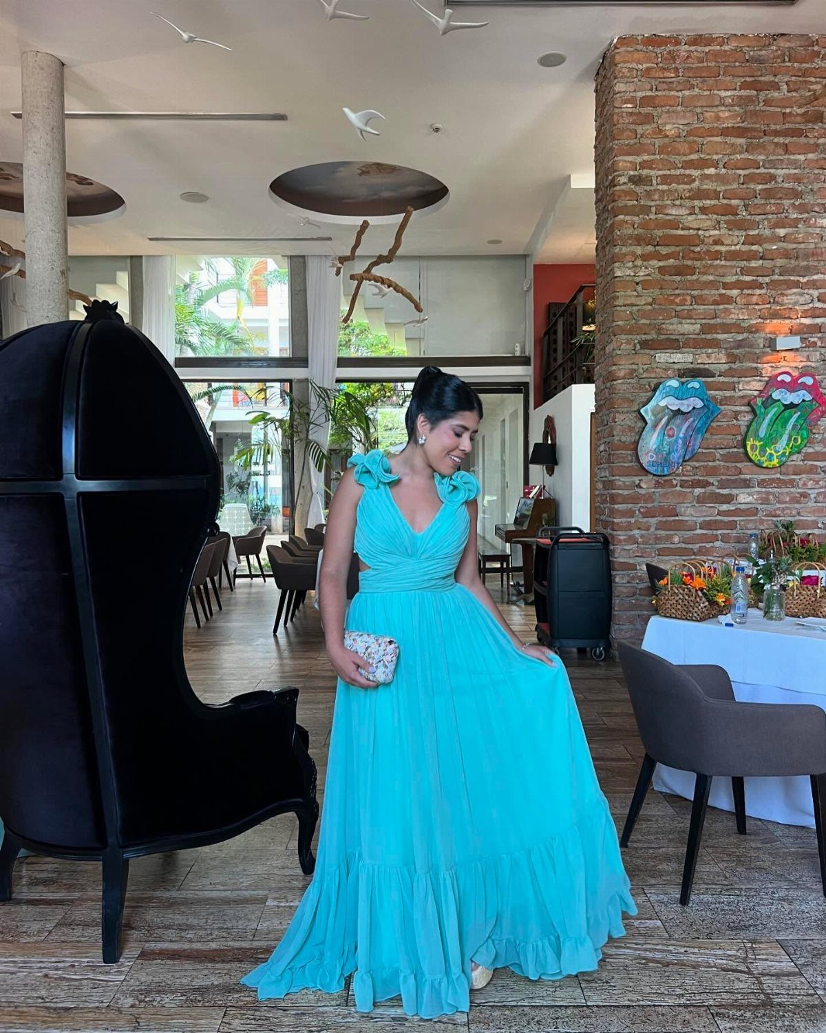 A woman wearing a long, bright turquoise ruffled maxi dress standing in a modern room.