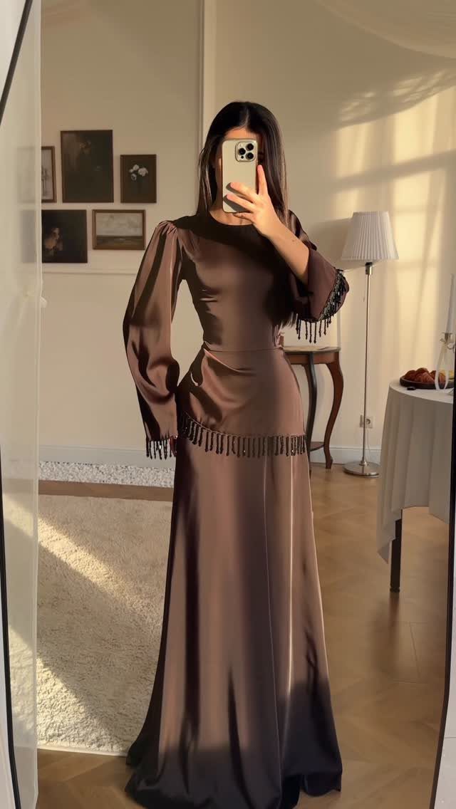 Woman in a long-sleeved brown satin maxi dress posing for a mirror selfie.