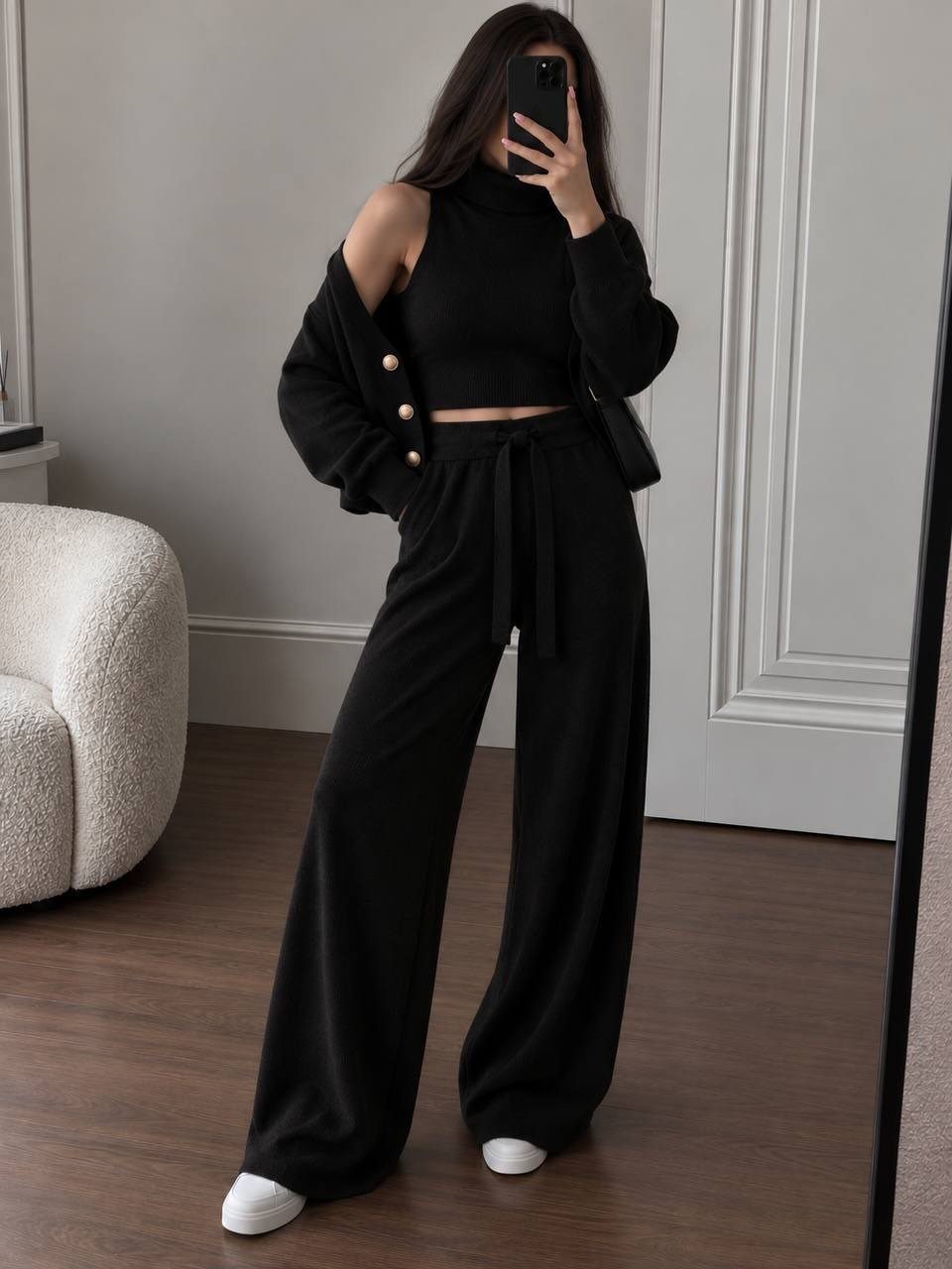 Woman posing in a black sleeveless turtleneck, wide-leg trousers, and a jacket while taking a mirror selfie.