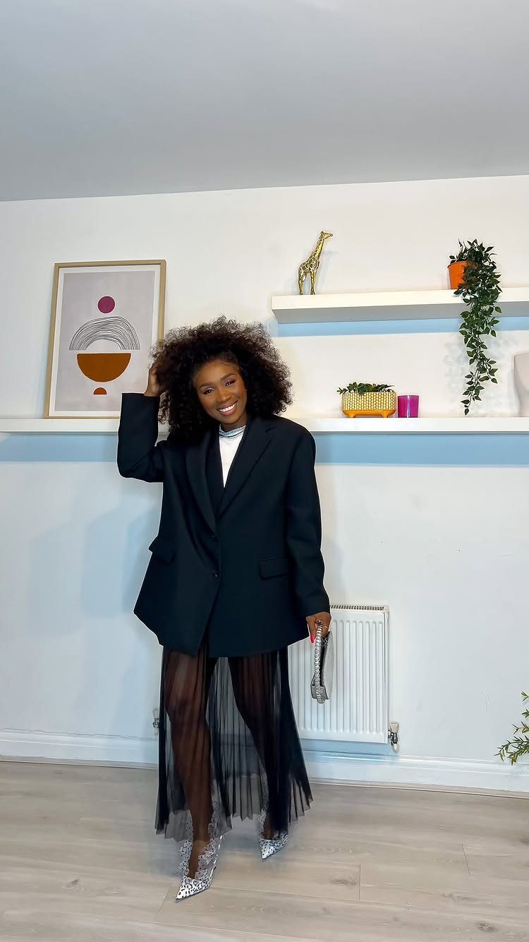A smiling woman posing in a black blazer and a sheer black tulle skirt.