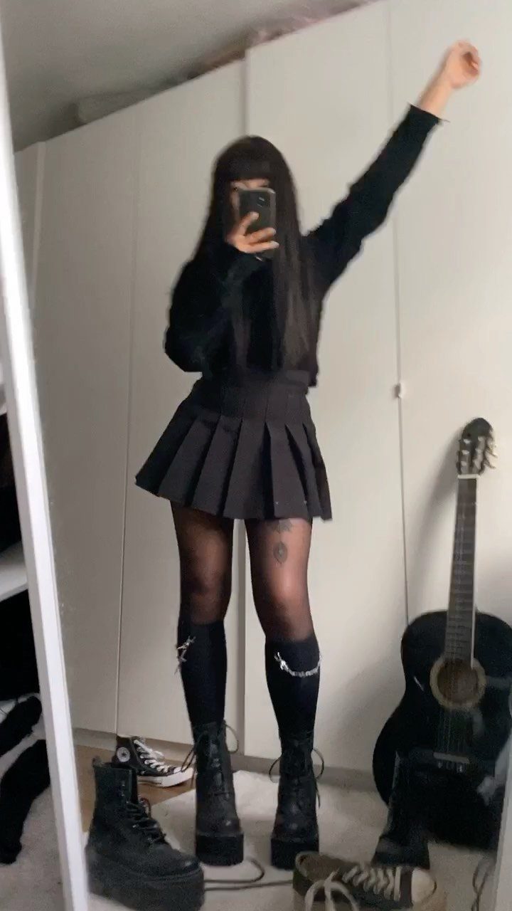 Person wearing an all-black outfit with a pleated skirt, tights, and platform boots.