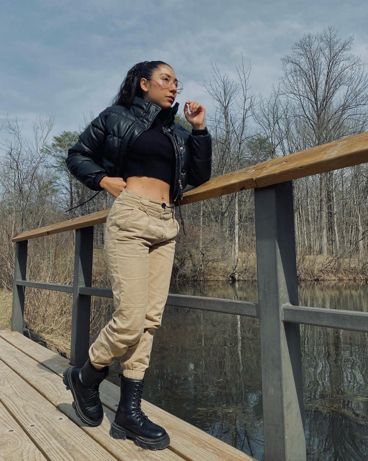 A woman in a black puffer jacket and tan cargo pants standing on a wooden bridge.