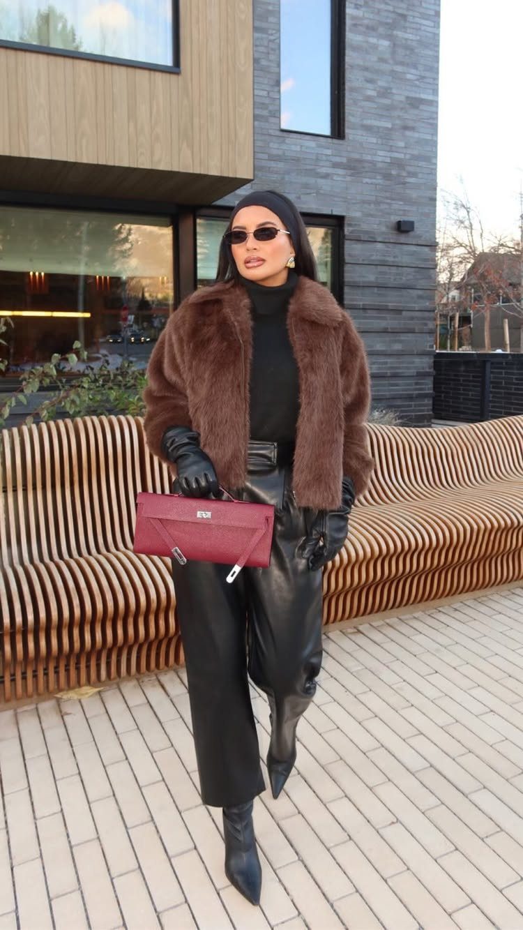 Woman in a brown faux fur jacket, black turtleneck, and black leather pants standing outdoors.