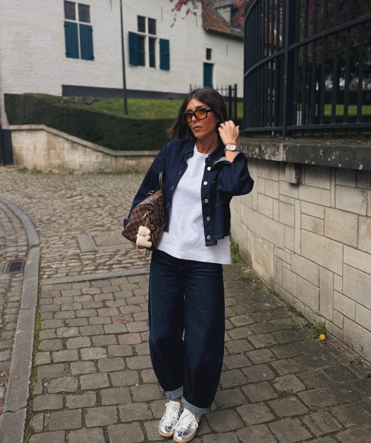 Woman wearing a dark denim jacket, white t-shirt, and wide-leg denim jeans on a cobblestone street.