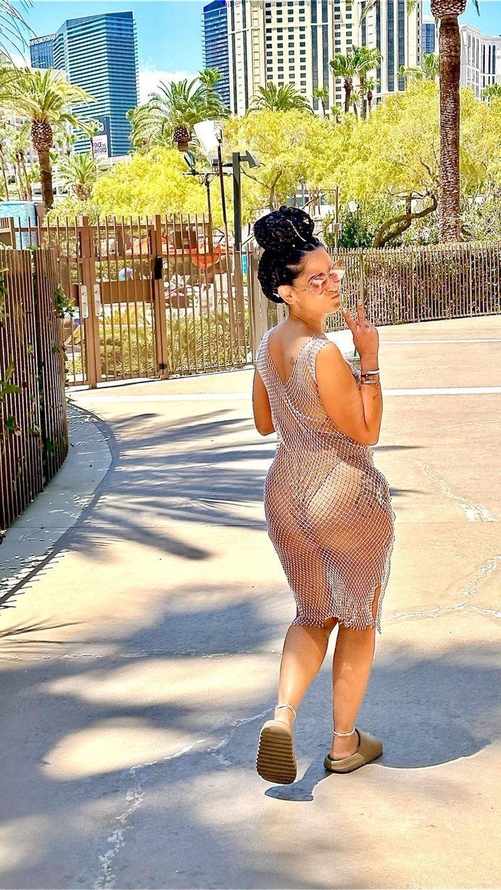 Woman wearing a sparkling silver mesh cover-up posing on a sunny walkway with palm trees.