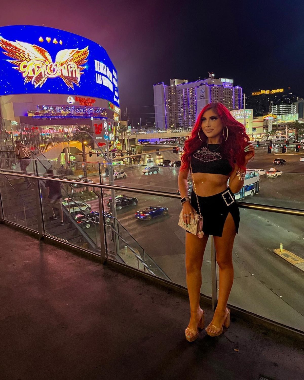 Woman in a black crop top and mini skirt posing against the Las Vegas skyline at night.