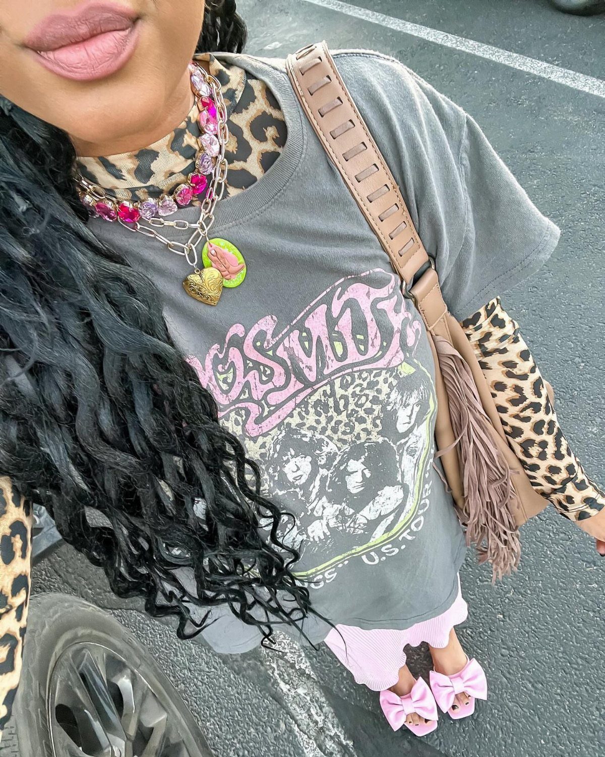 Person wearing leopard print sleeves, chunky pink necklaces, and a tan fringed crossbody bag.