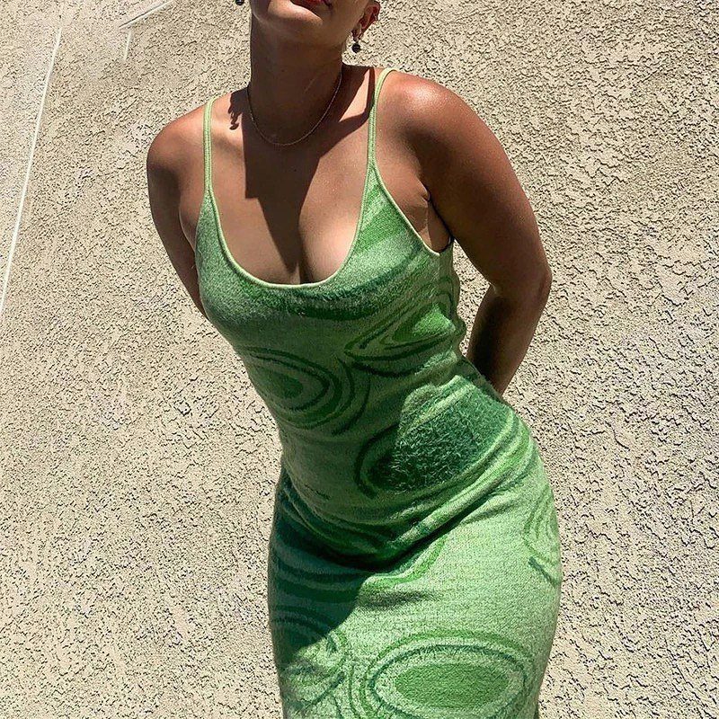 A person wearing a lime green patterned bodycon dress standing against a textured wall.