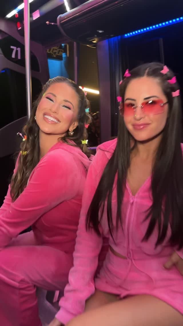 Two women in pink velour tracksuits smiling while wearing butterfly clips in their hair.