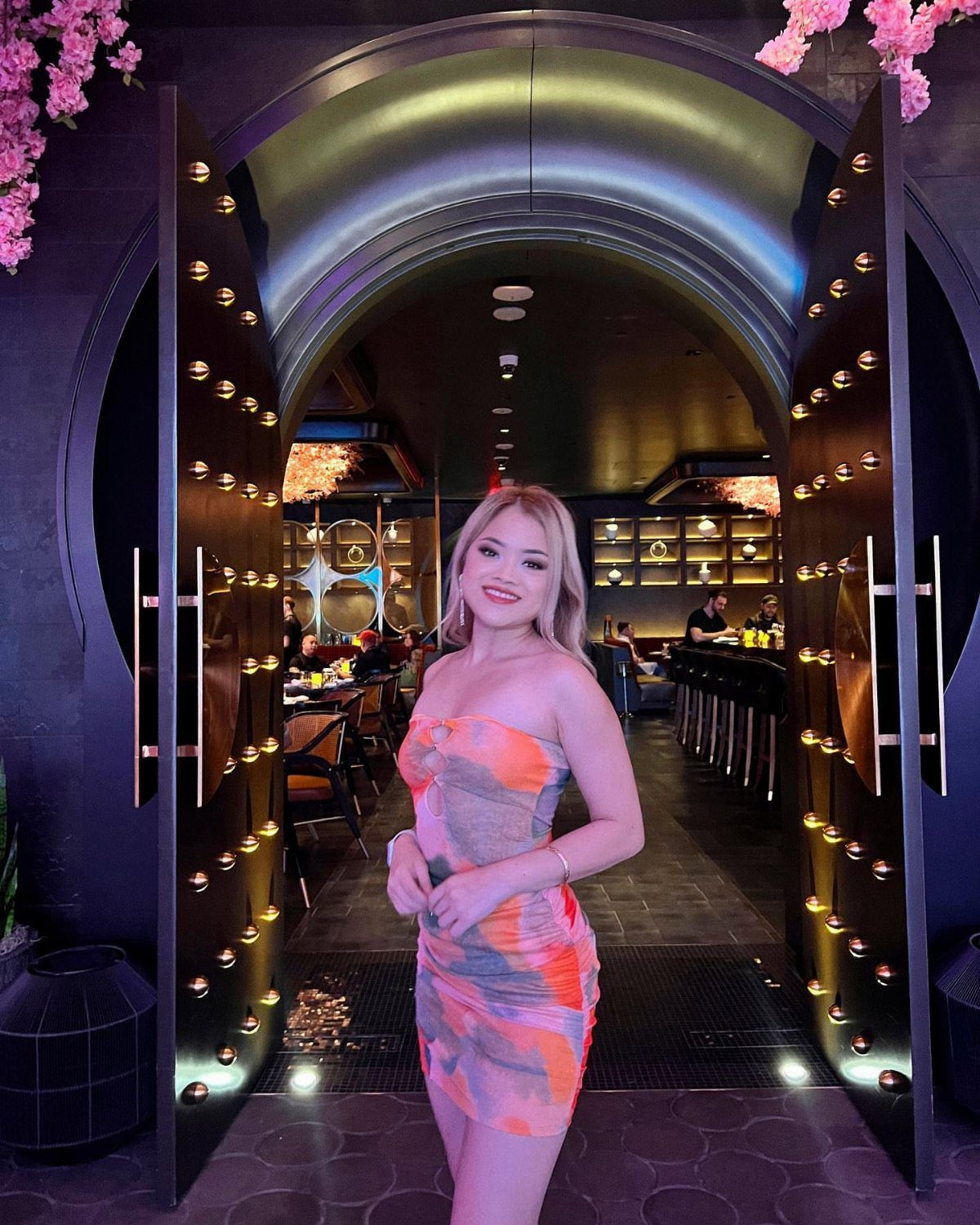 Blonde woman in a colorful strapless mini dress standing in a club entrance.